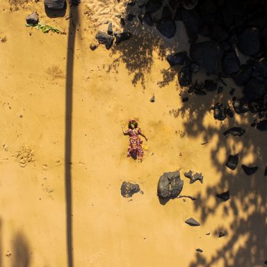 Une silhouette allongée sur un sol jaune avec des pierres et des ombres.