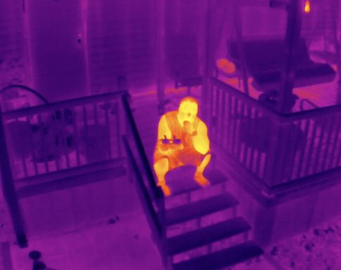 Personne assise sur des marches, visible en thermique avec des tons violets et jaunes.