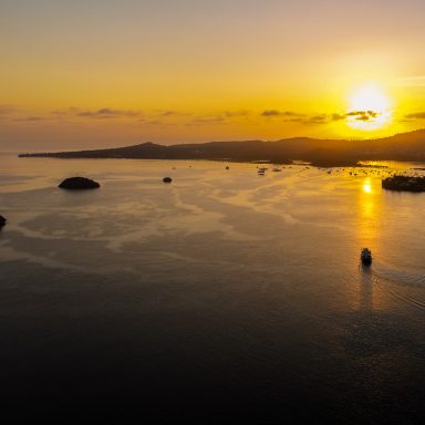 Coucher de soleil sur un paysage côtier avec silhouettes de montagnes et bateaux.